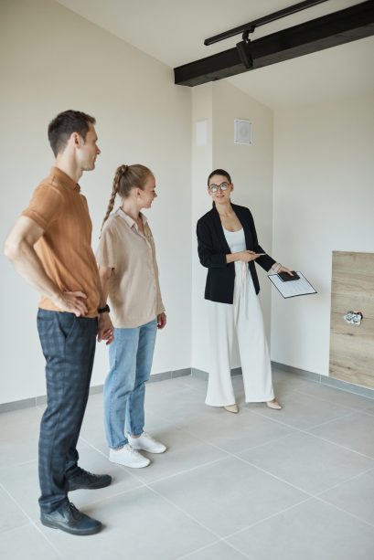 Full length portrait of female real estate agent giving apartment tour to young couple buying new property
