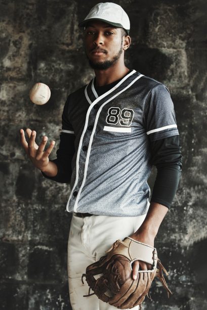 Baseball, sports and uniform with a man athlete on a dark background wearing a mitt while holding a.