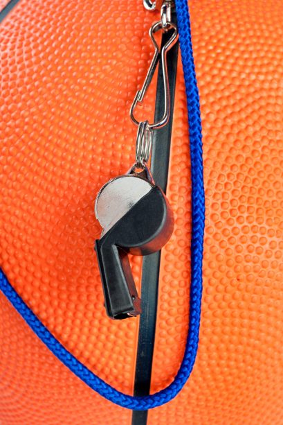 A basketball referee's whistle draped over an orange, rubber basketball. Good for sports inferences where rules are important.