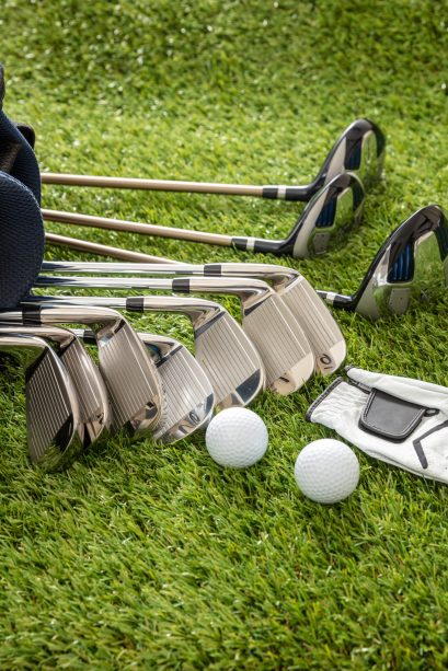 Golf equipment, sticks set in a bag glove and golfballs on green course lawn, close up vertical view. Golfing sport and club concept