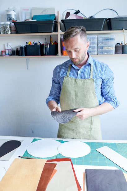Master man in an apron cut out leather goods in atelier