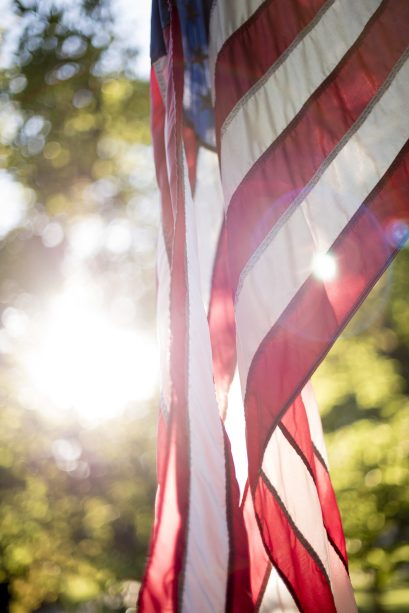 A vertical closeup shot of the united states flag with the sun shining in the background